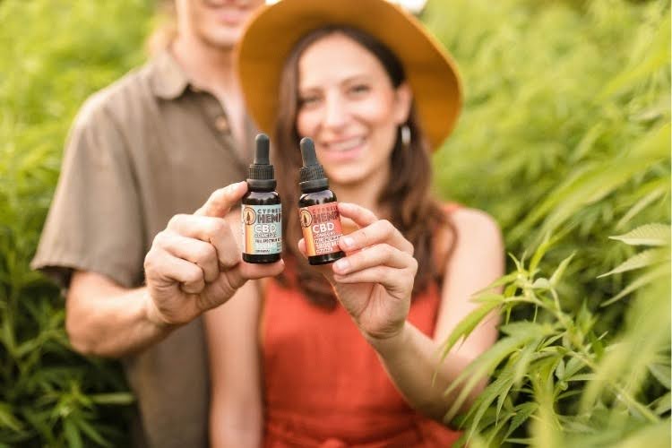 Couple holding two bottles of CBD oil outdoors