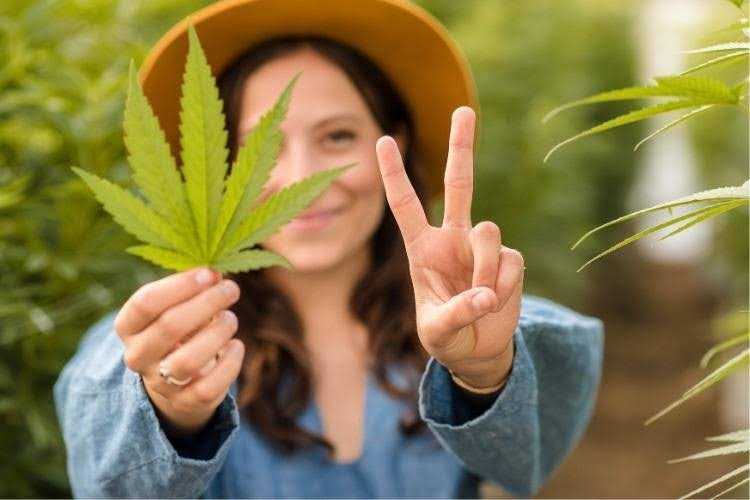Woman holding a cannabis leaf outdoors.